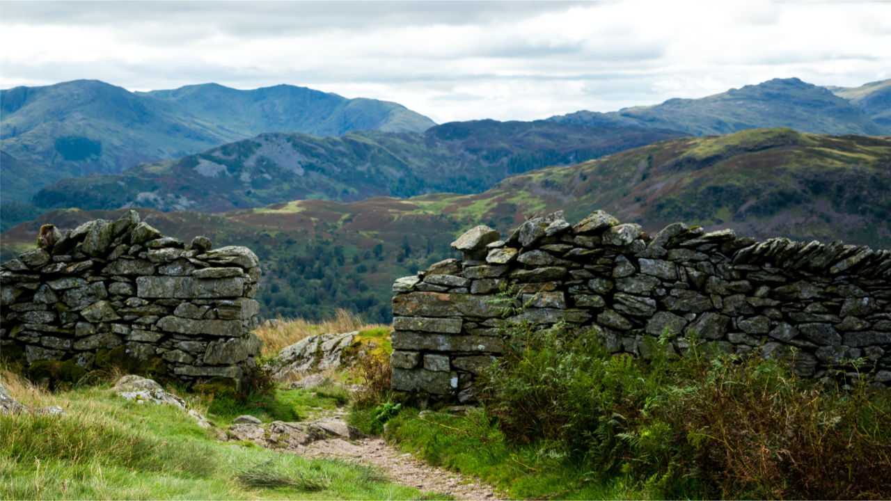Sky, mountains, and a pathway leading through a stone wall