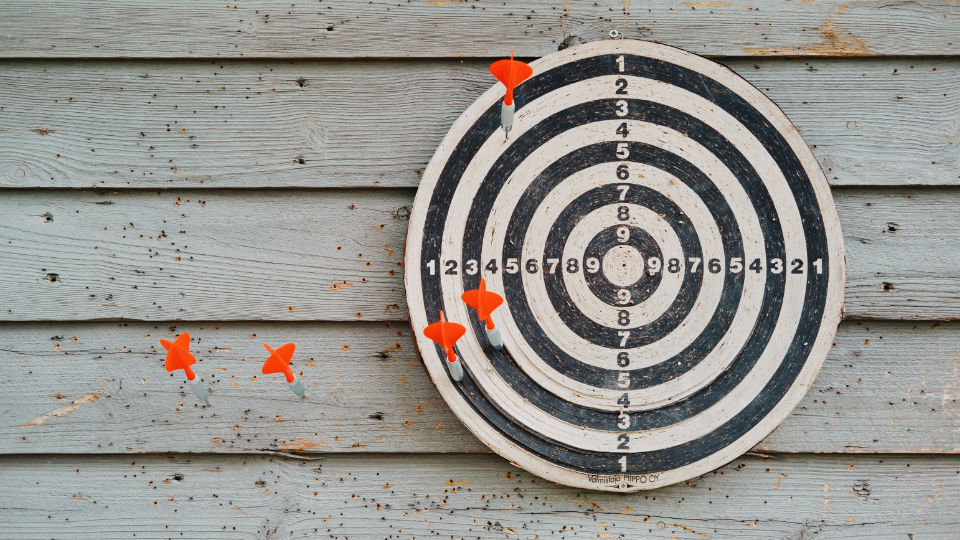 Black and white dartboard with five darts badly thrown