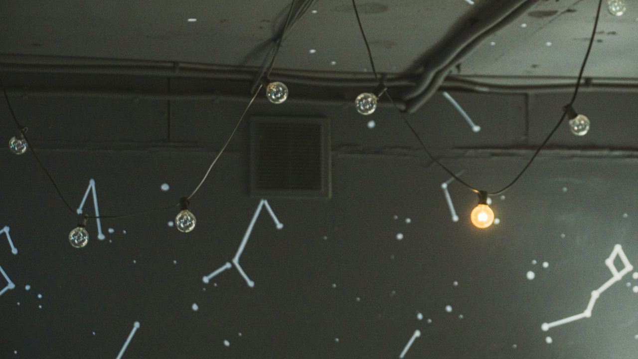 A string of light bulbs hanging from the ceiling, set against a gray interior with wallpaper patterned with constellations.